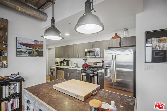 kitchen with washer / dryer, hanging light fixtures, stainless steel appliances, and sink