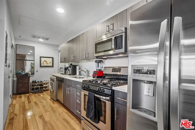 kitchen with washer / dryer, stainless steel appliances, light hardwood / wood-style floors, and sink