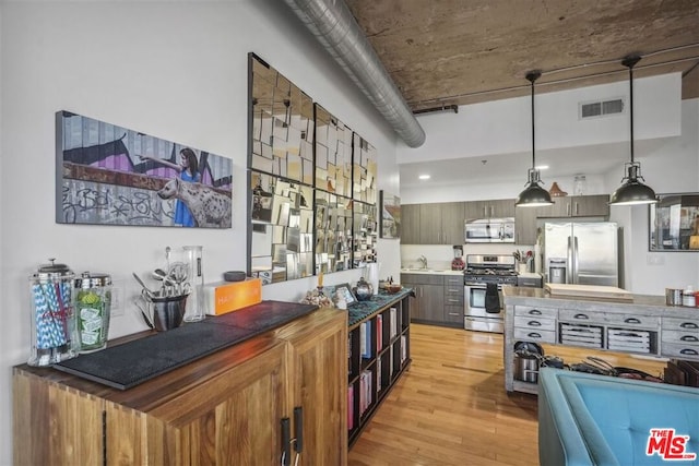 kitchen featuring sink, stainless steel appliances, hanging light fixtures, and light hardwood / wood-style flooring