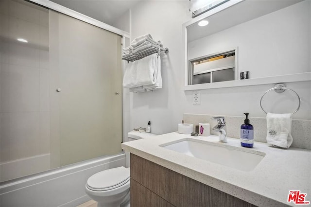 full bathroom featuring toilet, combined bath / shower with glass door, and vanity