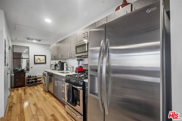 kitchen with washer / clothes dryer, sink, light hardwood / wood-style floors, and appliances with stainless steel finishes