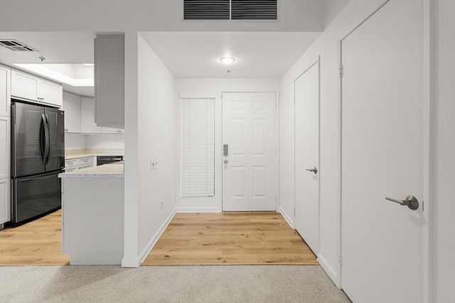 kitchen featuring stainless steel fridge, light wood-type flooring, backsplash, and white cabinetry