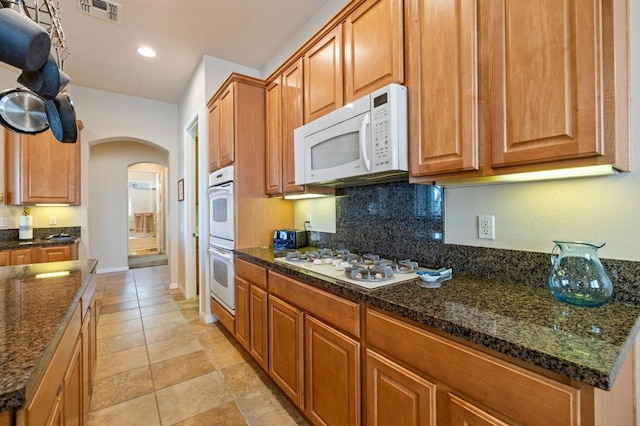 kitchen featuring white appliances, decorative backsplash, and dark stone counters