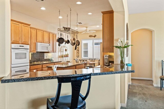 kitchen featuring white appliances, decorative backsplash, kitchen peninsula, a breakfast bar, and ceiling fan