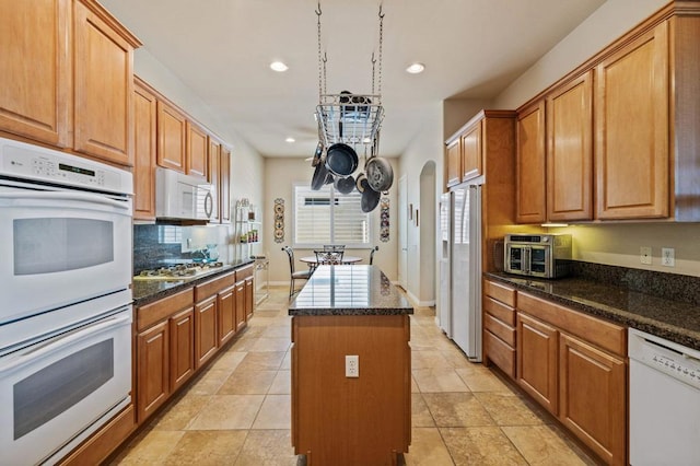 kitchen featuring dark stone counters, a center island, white appliances, and light tile patterned floors