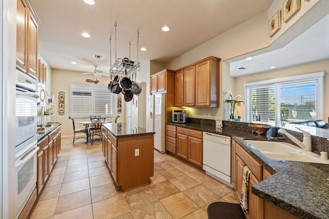 kitchen with white appliances, a kitchen island, dark stone countertops, sink, and ceiling fan