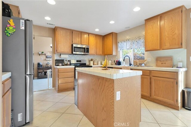 kitchen featuring tile countertops, a center island, decorative backsplash, light tile patterned floors, and stainless steel appliances