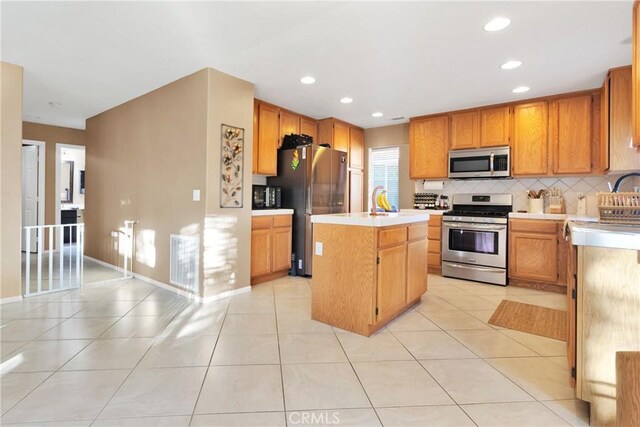 kitchen featuring decorative backsplash, light tile patterned flooring, an island with sink, and appliances with stainless steel finishes