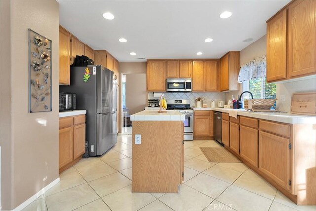 kitchen with tasteful backsplash, stainless steel appliances, sink, light tile patterned floors, and a kitchen island