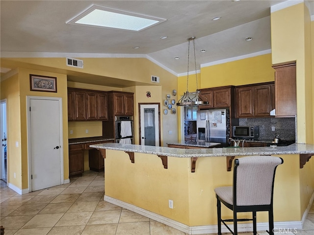 kitchen with a kitchen breakfast bar, vaulted ceiling with skylight, light stone countertops, appliances with stainless steel finishes, and kitchen peninsula