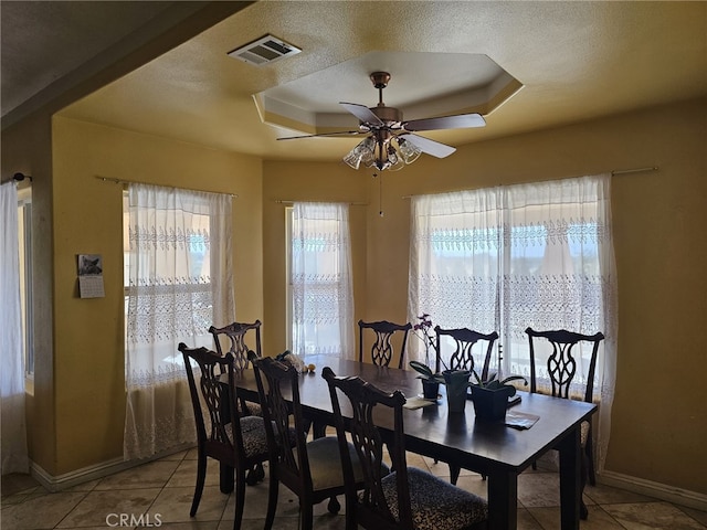 dining space featuring a tray ceiling, ceiling fan, light tile patterned floors, and a textured ceiling