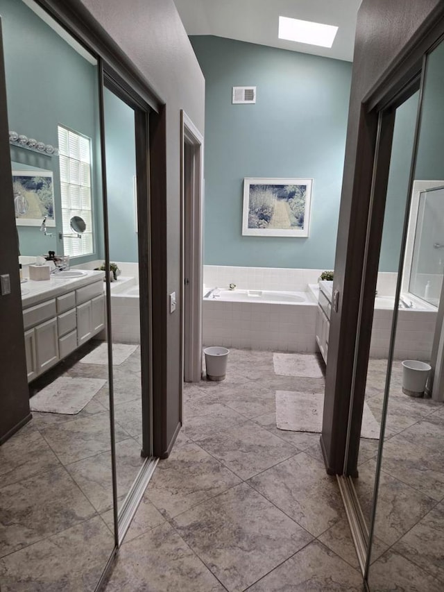 bathroom with vanity, a relaxing tiled tub, and lofted ceiling with skylight