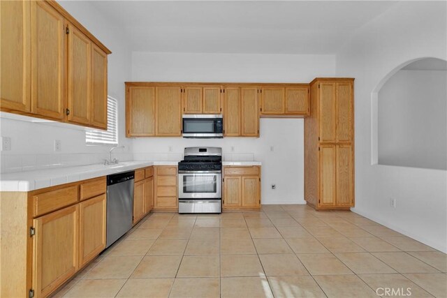 kitchen featuring sink, tile counters, light tile patterned flooring, and appliances with stainless steel finishes