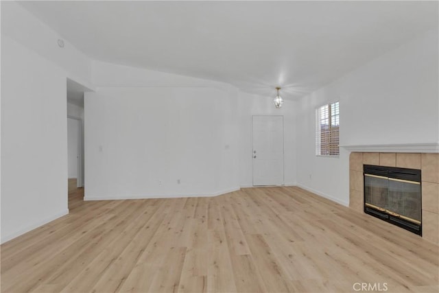 unfurnished living room featuring lofted ceiling, light wood-type flooring, and a tile fireplace