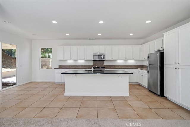 kitchen with white cabinetry, a center island with sink, light tile patterned floors, and stainless steel appliances