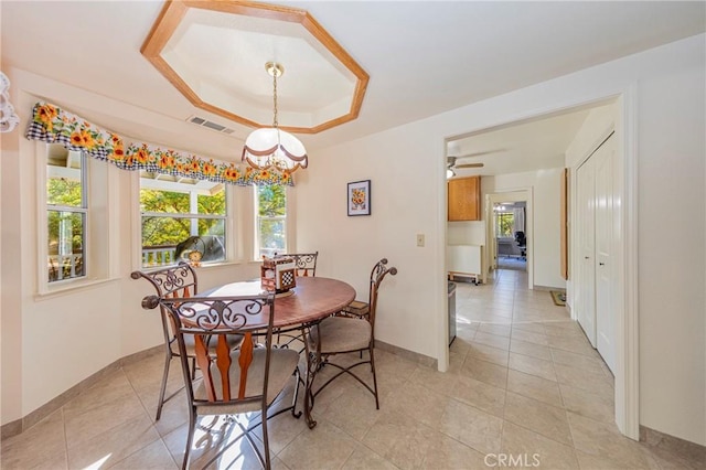 tiled dining room featuring ceiling fan with notable chandelier and a raised ceiling