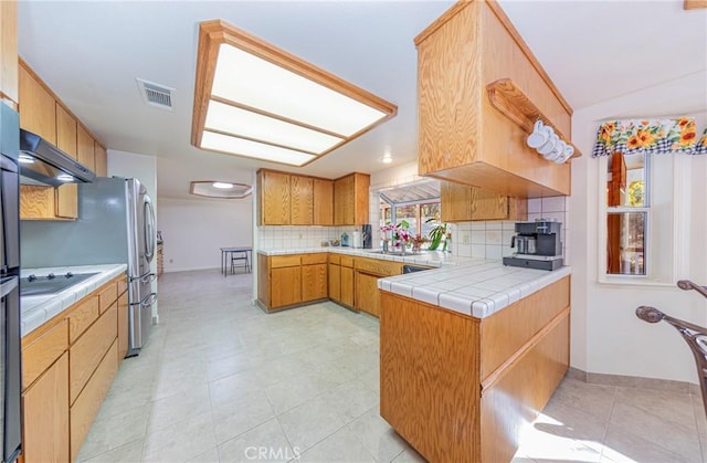 kitchen with tile countertops, decorative backsplash, light tile patterned floors, and kitchen peninsula