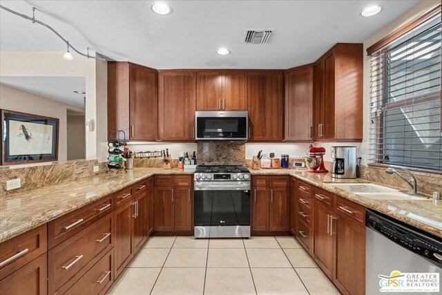 kitchen with kitchen peninsula, sink, light stone countertops, stainless steel appliances, and light tile patterned floors