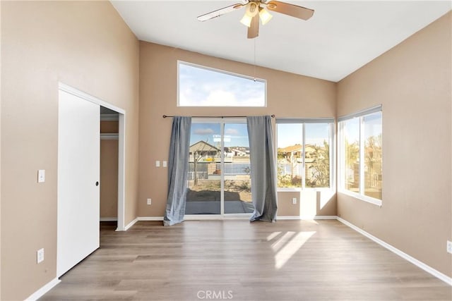 empty room with ceiling fan, high vaulted ceiling, and light hardwood / wood-style floors