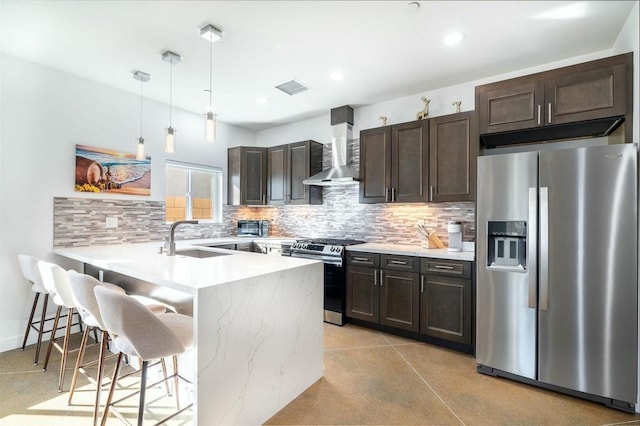 kitchen with wall chimney exhaust hood, a breakfast bar, stainless steel appliances, sink, and hanging light fixtures