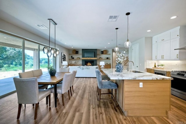 kitchen featuring a large fireplace, sink, white cabinets, stainless steel gas stove, and an island with sink