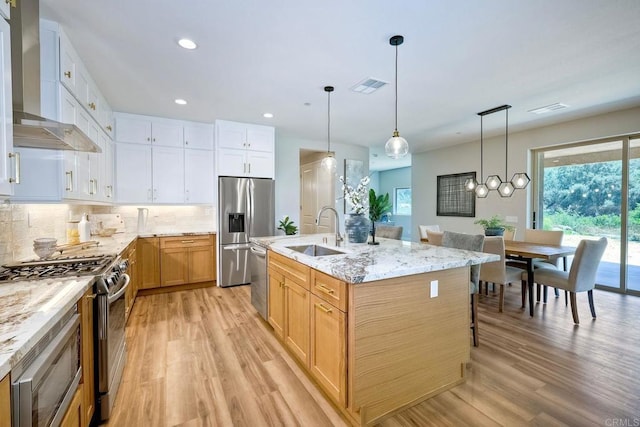 kitchen featuring white cabinets, sink, wall chimney exhaust hood, an island with sink, and stainless steel appliances