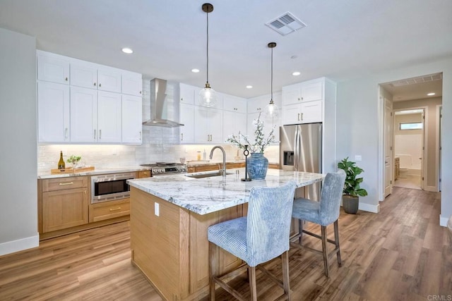 kitchen featuring white cabinetry, sink, wall chimney range hood, an island with sink, and appliances with stainless steel finishes