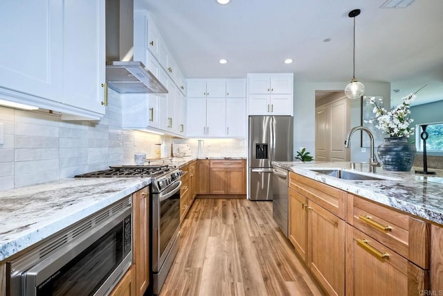 kitchen with appliances with stainless steel finishes, wall chimney range hood, pendant lighting, light hardwood / wood-style flooring, and white cabinetry