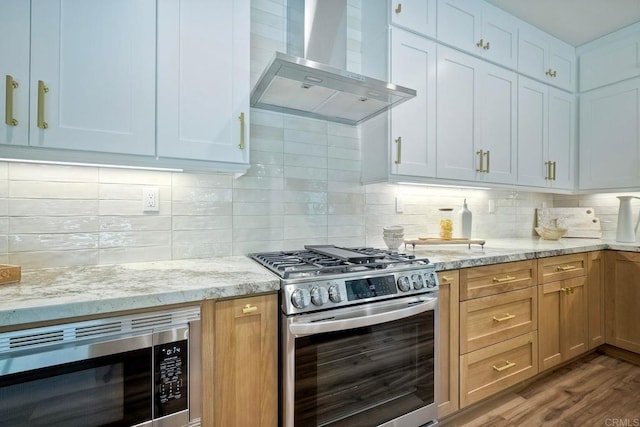 kitchen with white cabinetry, light stone countertops, wall chimney exhaust hood, hardwood / wood-style floors, and appliances with stainless steel finishes