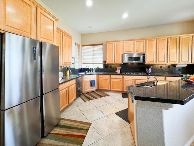 kitchen with stainless steel appliances, dark stone counters, light brown cabinetry, kitchen peninsula, and light tile patterned floors