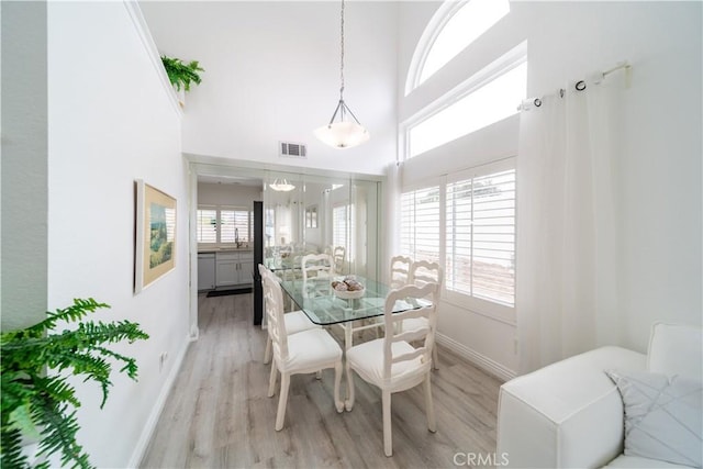 dining room featuring a towering ceiling, sink, and light hardwood / wood-style floors