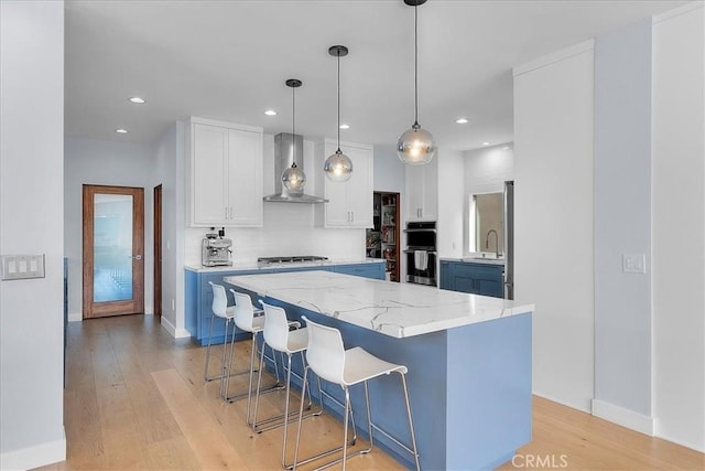 kitchen featuring a center island, wall chimney exhaust hood, pendant lighting, light hardwood / wood-style floors, and white cabinets