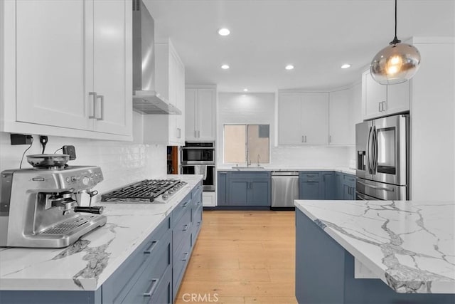 kitchen featuring appliances with stainless steel finishes, wall chimney exhaust hood, decorative light fixtures, white cabinets, and light hardwood / wood-style floors