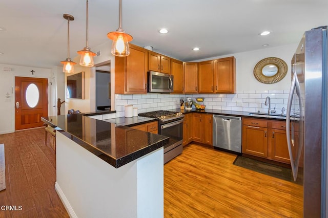 kitchen with kitchen peninsula, light wood-type flooring, stainless steel appliances, sink, and pendant lighting