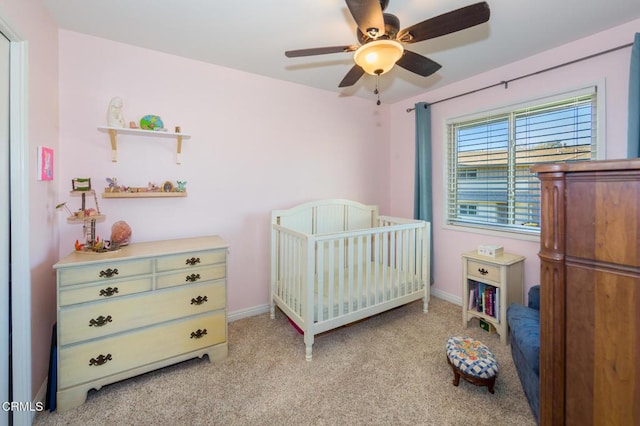 bedroom featuring ceiling fan, a crib, and light carpet