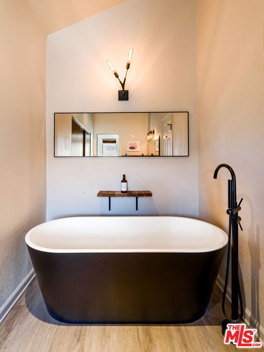 bathroom with a bath, hardwood / wood-style flooring, and lofted ceiling