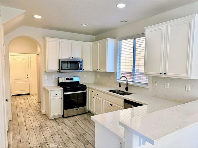 kitchen with kitchen peninsula, sink, white cabinetry, appliances with stainless steel finishes, and light stone counters