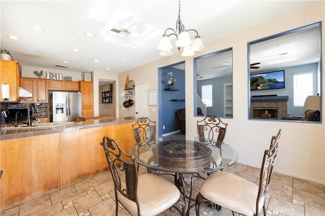 dining space with a tiled fireplace, sink, and ceiling fan with notable chandelier