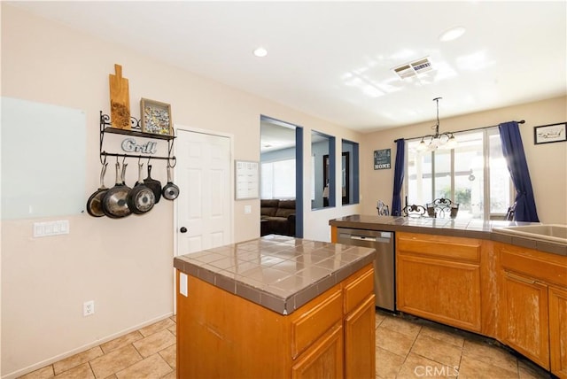 kitchen featuring a center island, stainless steel dishwasher, a notable chandelier, tile countertops, and decorative light fixtures