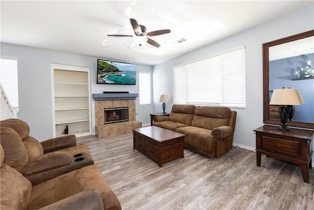 living room featuring a tile fireplace, light hardwood / wood-style flooring, and ceiling fan