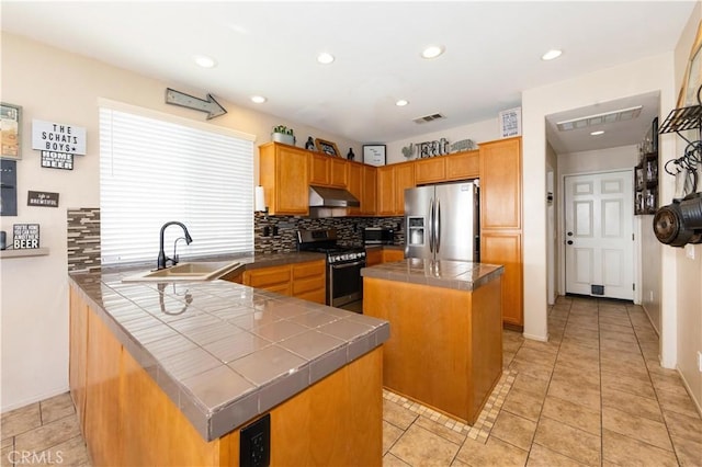 kitchen featuring tasteful backsplash, stainless steel appliances, sink, a kitchen island, and tile counters