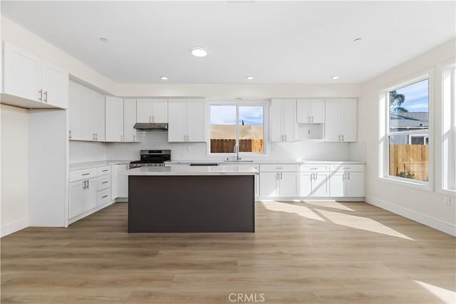 kitchen with stainless steel range, white cabinets, light hardwood / wood-style floors, and plenty of natural light