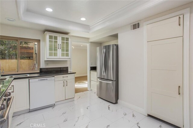 kitchen featuring white cabinetry, appliances with stainless steel finishes, ornamental molding, and a raised ceiling