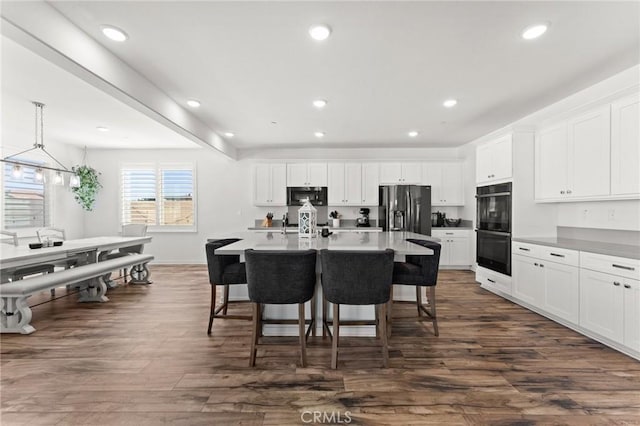 kitchen featuring a breakfast bar area, stainless steel fridge with ice dispenser, an island with sink, hanging light fixtures, and white cabinets