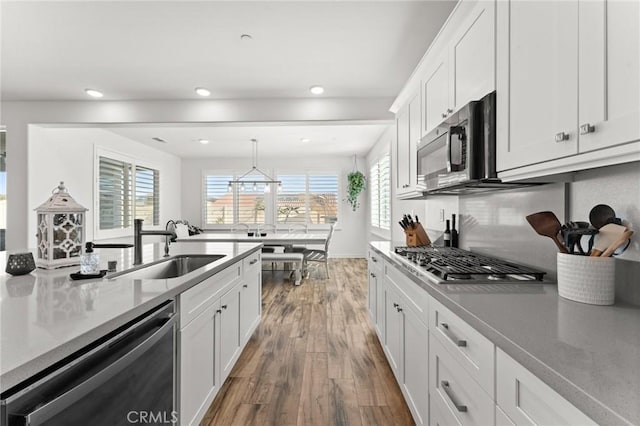 kitchen with dishwasher, pendant lighting, white cabinets, wood-type flooring, and sink