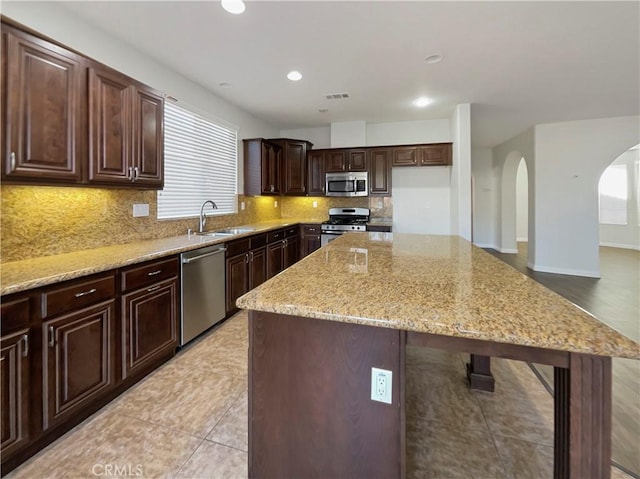 kitchen with light stone counters, sink, stainless steel appliances, and a kitchen island