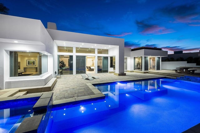 pool at dusk featuring a patio and a hot tub