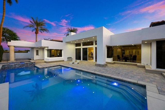 pool at dusk featuring an in ground hot tub and a patio