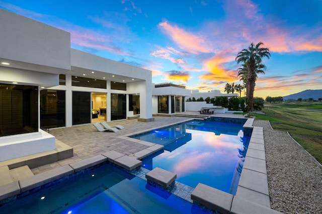 pool at dusk with a mountain view, a patio area, and a jacuzzi