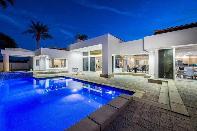 pool at night featuring a patio area and an in ground hot tub